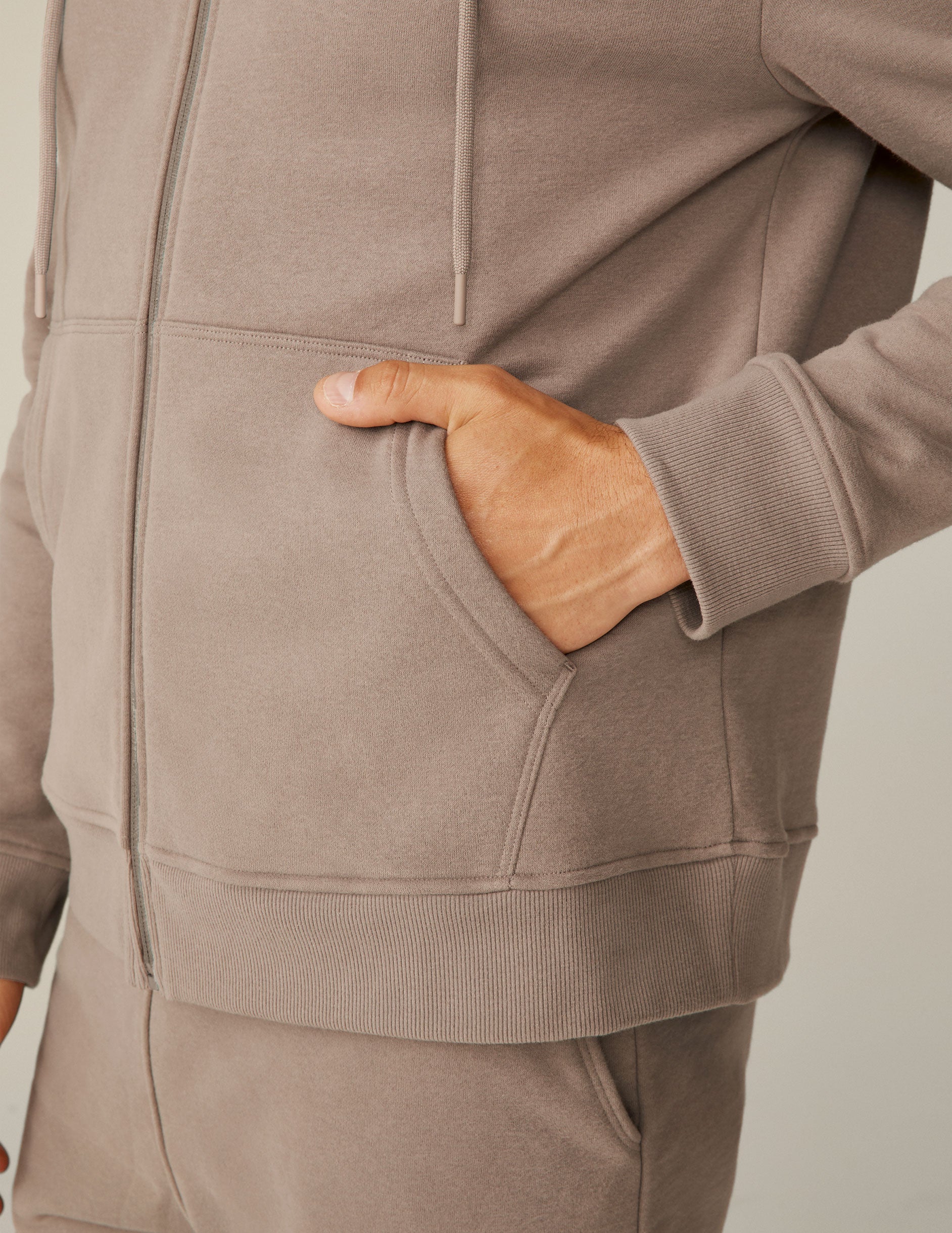 model is wearing a brown men's zip-up hooded jacket.