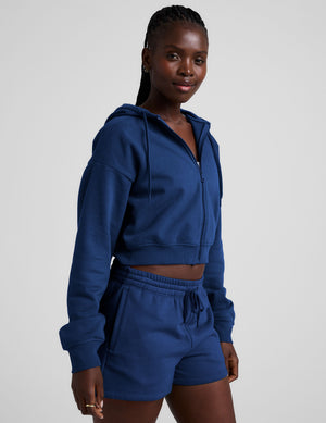 Woman wearing a blue zip-up hoodie and fleece shorts on a plain background.
