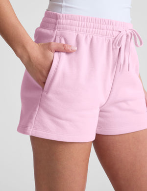 Person wearing pink fleece shorts on a plain background. 