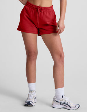 woman wearing a red sweat shorts against a plain background. 
