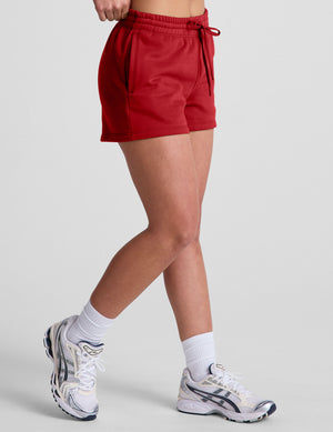 woman wearing a red sweat shorts against a plain background. 