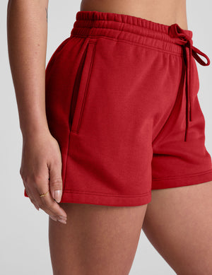 woman wearing a red sweat shorts against a plain background. 