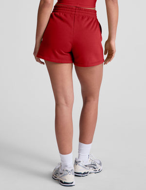 woman wearing a red sweat shorts against a plain background. 