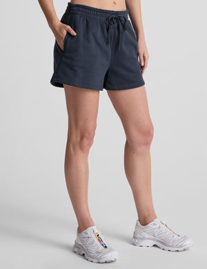 model wearing blue sweat shorts and white sneakers on a light gray background. 
