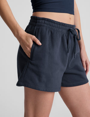 model wearing blue sweat shorts and white sneakers on a light gray background. 
