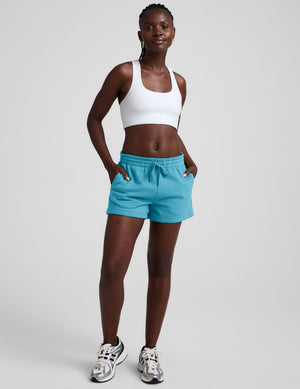 Woman wearing a white sports bra and blue shorts on a plain background. 