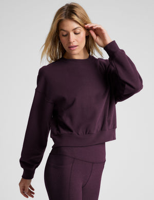 model wearing a purple fleece cropped crew neck sweatshirt and leggings on a light gray background. 