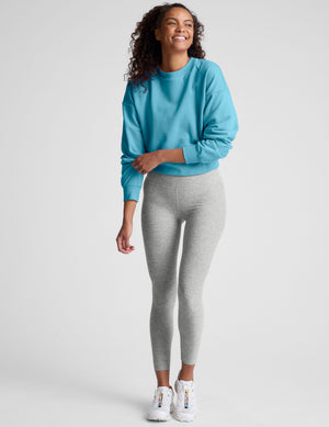 Woman wearing a blue sweatshirt and gray leggings on a plain background. 
