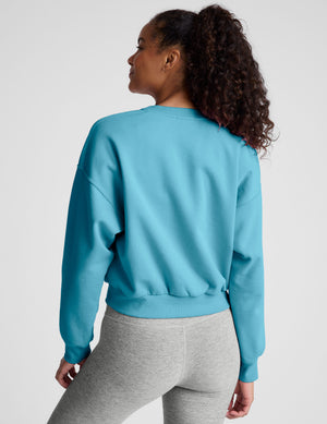 Woman wearing a blue sweatshirt and gray leggings on a plain background. 