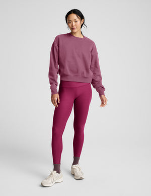Woman wearing a pink crew neck sweatshirt and leggings sitting on a plain background. 