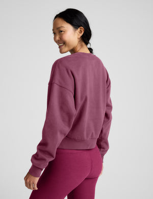 Woman wearing a pink crew neck sweatshirt and leggings sitting on a plain background. 