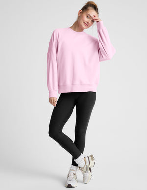 Woman wearing a pink oversized sweatshirt and black leggings on a plain background. 