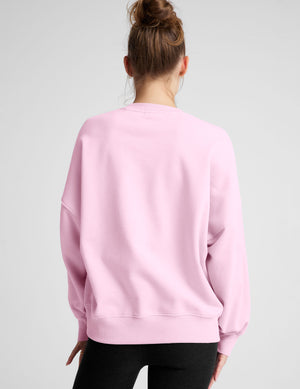 Woman wearing a pink oversized sweatshirt and black leggings on a plain background. 
