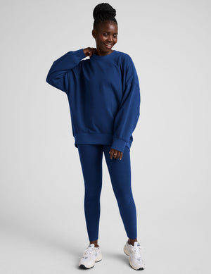Woman wearing a blue oversized sweatshirt and leggings on a plain background. 