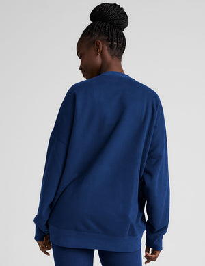 Woman wearing a blue oversized sweatshirt and leggings on a plain background. 