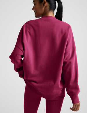 Woman wearing a red crewneck sweatshirt and leggings against a light gray background. 