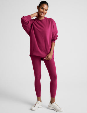 Woman wearing a red crewneck sweatshirt and leggings against a light gray background. 