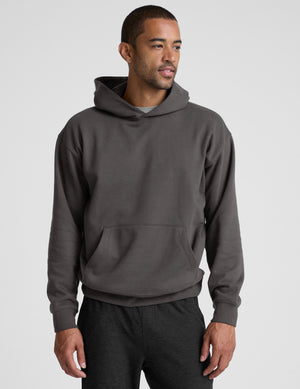 Man wearing a gray hoodie and pants on a light gray background. 