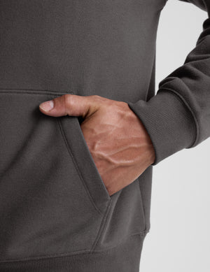 Man wearing a gray hoodie and pants on a light gray background. 