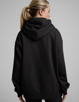 Woman wearing a black oversized hoodie and black leggings against a plain background. 