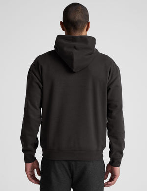 man wearing a black hoodie on a plain background. 