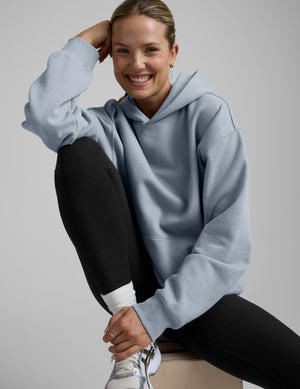 Woman wearing a light blue hoodie and black leggings on a gray background. 