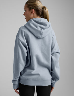 Woman wearing a light blue hoodie and black leggings on a gray background. 