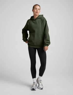 woman wearing a green oversized hoodie and black leggings on a gray background. 