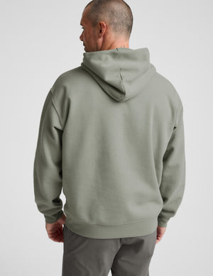 Man wearing a green hoodie and gray pants on a light gray background. 