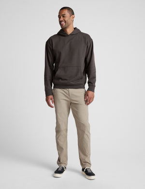 Man wearing a dark brown hoodie and beige pants on a white background