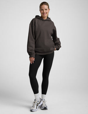 Woman wearing a brown hoodie and black leggings on a white background