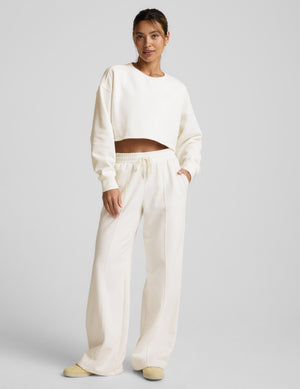 Woman wearing a white cropped sweatshirt and pants on a light gray background. 