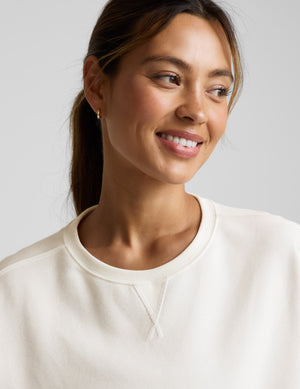 Woman wearing a white cropped sweatshirt and pants on a light gray background. 