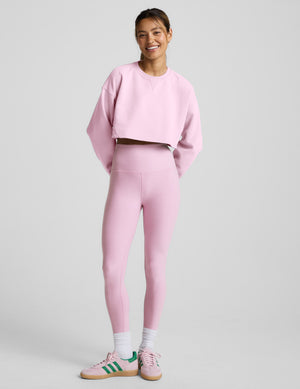 Woman wearing a pink cropped sweatshirt and leggings on a plain background. 