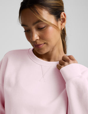 Woman wearing a pink sweatshirt and pants on a light gray background. 