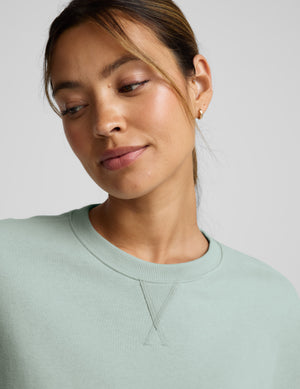 Woman wearing a light blue cropped sweatshirt and pants on a plain background. 