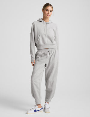 Woman wearing a gray hoodie and pants on a light gray background. 