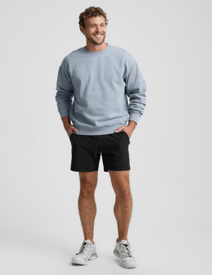 Man wearing a light blue sweatshirt and black shorts on a plain background. 