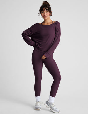 model wearing a dark purple long-sleeve boat neck sweater and leggings on a light gray background. 