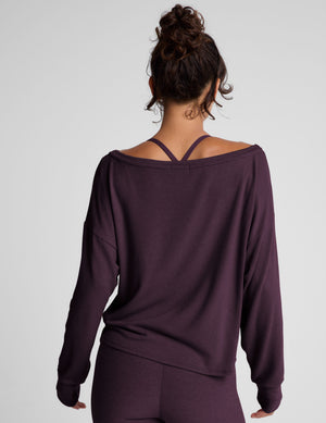 model wearing a dark purple long-sleeve boat neck sweater and leggings on a light gray background. 