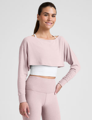 woman wearing a pink long-sleeve crop shrug and leggings on a plain background. 
