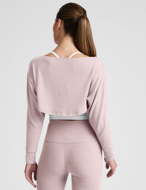 woman wearing a pink long-sleeve crop shrug and leggings on a plain background. 