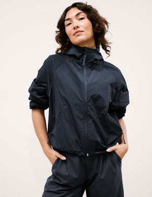 Woman wearing a blue hooded jacket and pants against a plain background. 