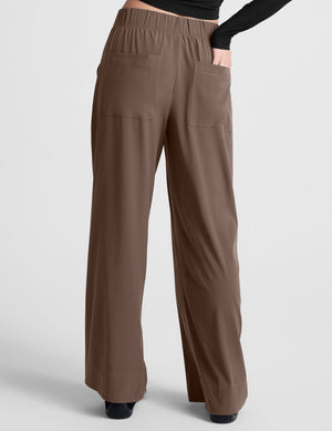 Woman wearing Brown Easy Wide Leg Pant with back pockets, paired with a black long-sleeve top. Rear view.