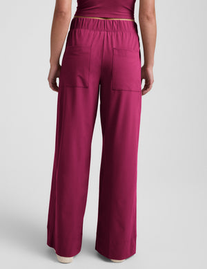 Woman wearing a magenta tank top and magenta wide leg pants against a plain background. 