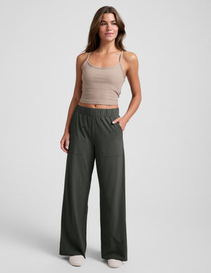 Woman wearing a brown tank top and green wide leg pants against a plain background. 