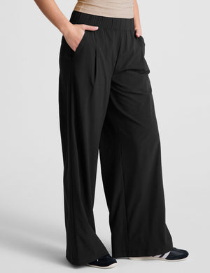 Flowy black Easy Wide Leg Pant with a pleated front and elastic waist, styled with hands in pockets for a relaxed fit.