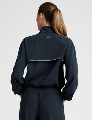 model wearing a blue track jacket with white piping detail on a light gray background. 