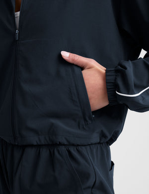 model wearing a blue track jacket with white piping detail on a light gray background. 