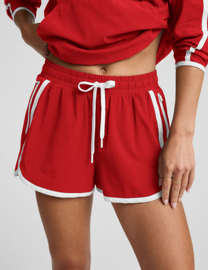 Woman in a red quarter zip jacket and shorts with white trim against a plain background. 